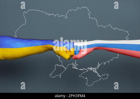 Russian-Ukrainian war. People hitting each other with hands painted in colors of Ukrainian and Russian flags against outline map of Ukraine, closeup Stock Photo