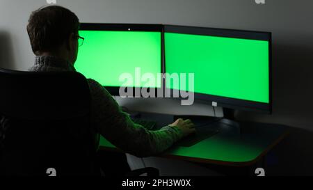 Late Evening in Creative Office: Professional Photographer Works on a Desktop Computer with Two Green Mock-up Screens. Modern Studio Office with Hanging Lightbulbs. High quality photo Stock Photo