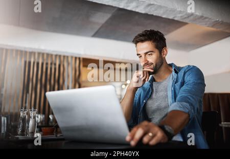 Log in and get it done. a handsome young man using a laptop in a coffee shop. Stock Photo