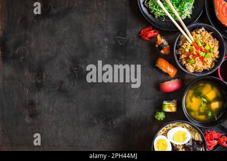 Sushi and japanese food on dark background. Sushi rolls, hiyashi wakame, miso soup, ramen, fried rice with vegetables, nigiri, salmon steak, soy Stock Photo