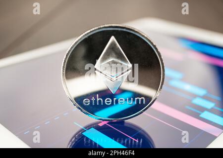 close-up photo of ether cryptocurrency physical coin on the tablet computer showing stock market charts. trading ether cryptocoin concept on the woode Stock Photo