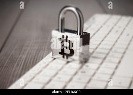 padlock with bitcoin symbol and white computer keyboard on the wooden office table. blockchain technology concept Stock Photo
