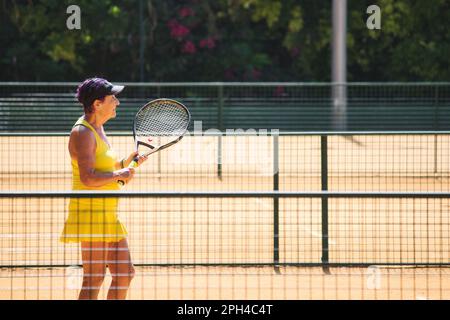 Atlanta, Georgia / USA - June 11 2022: A senior woman holding a tennis racket in a tennis court wearing summer sports clothing Stock Photo