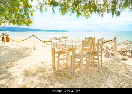 Beach restaurant with all white colored furniture in front of the fascinating golden turquoise colors of the sand and sea. Bright sunny day. Stock Photo