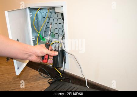 The router box is open, the human hand holds a screwdriver, there is a black router next to it Stock Photo
