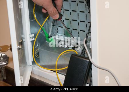 The router box is open, the human hand holds a screwdriver, there is a black router next to it Stock Photo