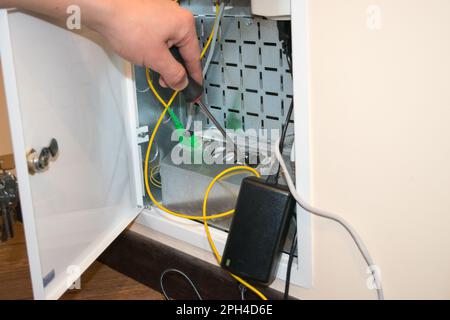 The router box is open, the human hand holds a screwdriver, there is a black router next to it Stock Photo