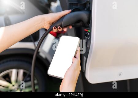 Hands with smartphone and charging plug on a background of electric car . White screen, you can add your content here. High quality photo Stock Photo