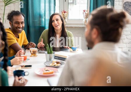 Group of multiracial friends studying together in a cozy cafeteria, enjoying tea, coffee and biscuits during their break and having a great time socia Stock Photo
