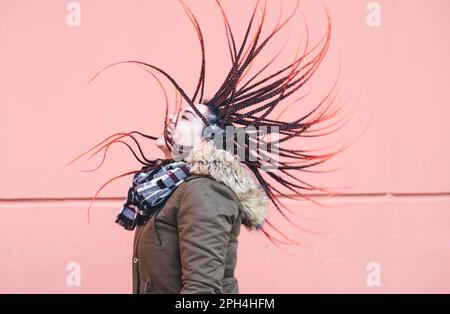 Close up of young woman with colorful flying braided dreads on coral background Stock Photo