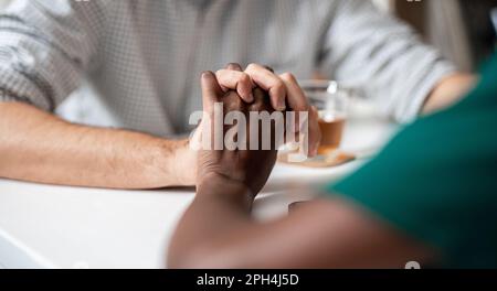 Close up of young couple hold hands at tea room in the city.  Multiracial couple having tender close moment together Stock Photo