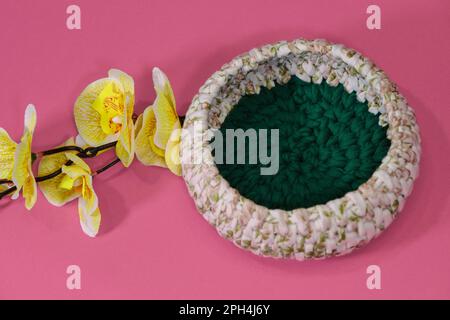 Green and white round box for small things made of thread crocheted, handmade art. Nearby is branch of yellow orchid flowers. Crochet Home Basket on Stock Photo