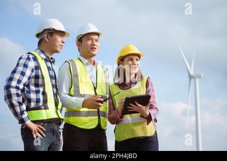 Team of asian engineers discussing and checking turbines on wind turbine farm. Renewable energy technology and sustainability. Stock Photo