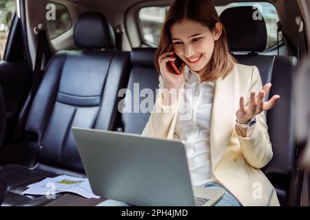Businesswoman talking on the mobile phone and using the laptop in the car. Stock Photo