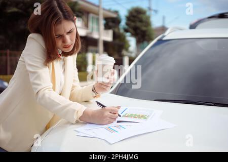 Busy woman is in a hurry, she does not have time, she is going to talk on the phone on the go. Businesswoman doing multiple tasks On the hood of the c Stock Photo