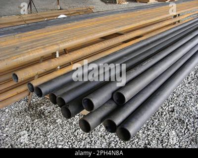 Storage of long plastic and steel pipes on the construction site, crushed stone floor. Building materials and structures. Stock Photo