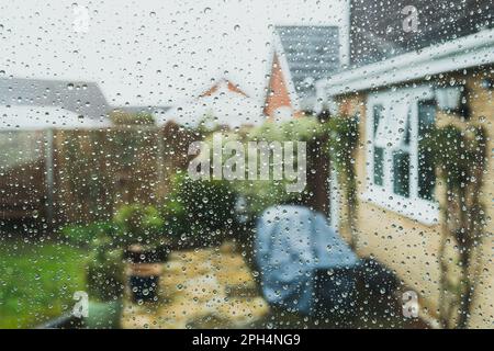 Shallow focus of raindrops seen on a conservatory window. Looking out to a patio area, seen during a rainstorm. Stock Photo