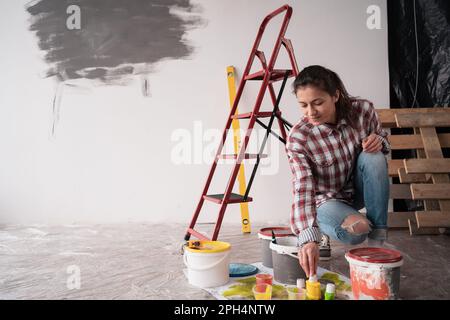 Woman working making home repair painting wall choose paint cans and color palette samples on floor Stock Photo