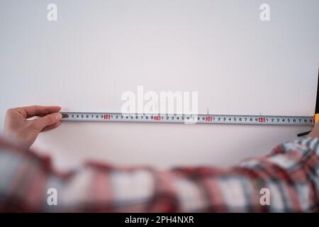 Female workman using tape measure for home renovation. Woman taking measure on the white wall. Measures wall with construction tape during home Stock Photo