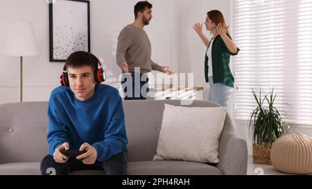 Teenage boy playing videogame while his parents arguing on background. Problems at home Stock Photo