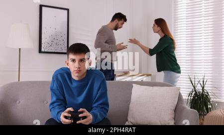 Teenage boy playing videogame while his parents arguing on background. Problems at home Stock Photo