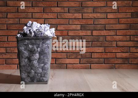 Trash bin full of paper on floor near brick wall, space for text. Recycling rubbish Stock Photo