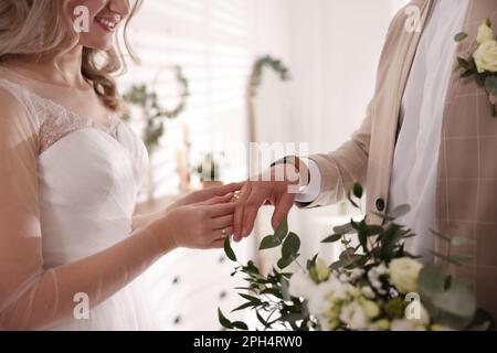 Groom and bride exchanging wedding rings indoors, closeup view Stock Photo