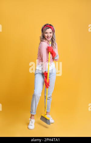 Beautiful young woman with floor brush singing on orange background Stock Photo