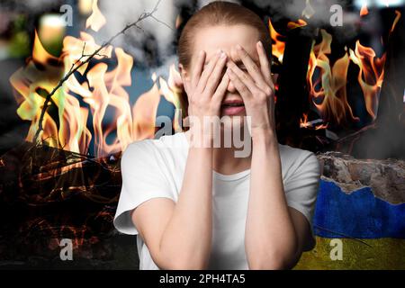 Upset woman near wall of ruined building painted in color of national flag on fire. Stop war in Ukraine Stock Photo