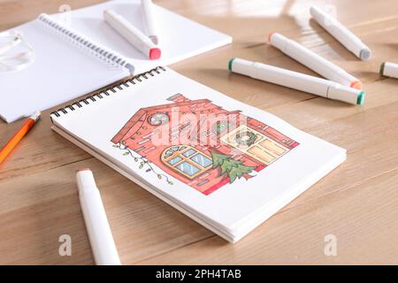 Sketchbook with beautiful drawing of house and felt tip pens on wooden table Stock Photo