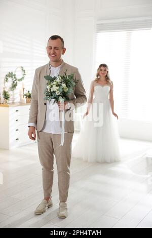 Groom with closed eyes waiting for his lovely bride indoors. First meeting at wedding day Stock Photo