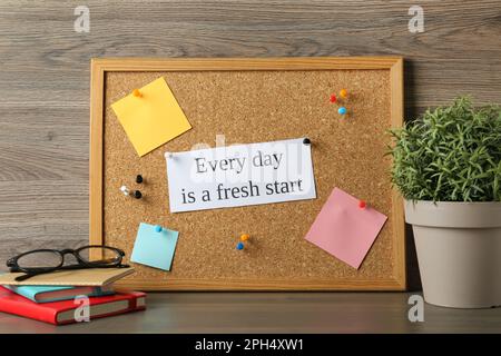 Cork board with motivational quote Every Day is a Fresh Start, stationery and plant on wooden table Stock Photo