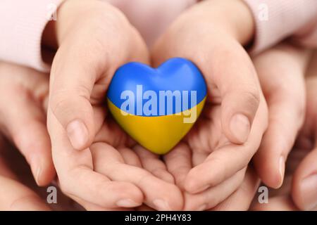 Stop war in Ukraine. Family holding heart shaped toy with colors of Ukrainian flag in hands, closeup Stock Photo