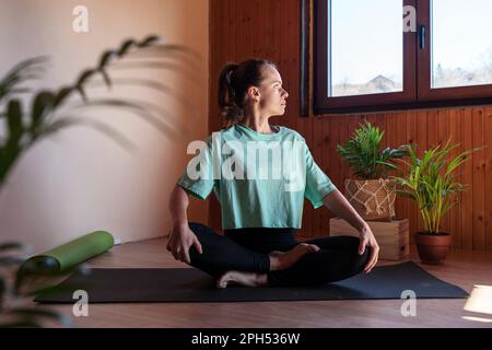 Woman sitting on yoga mat at home and meditating Stock Photo