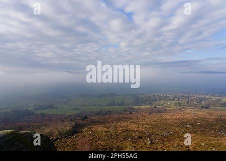 Down in the Hope Valley heavy dark fog and low cumulus cloud hang over Curbar village. Stock Photo