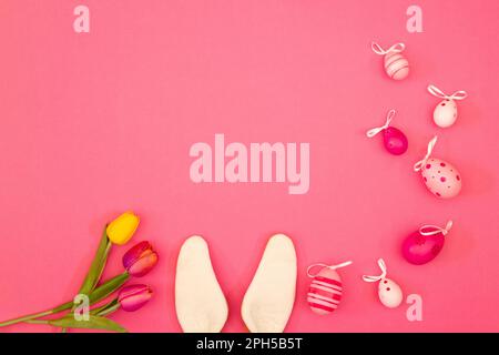Pink backdrop with Easter eggs, bunny ears, flowers and blank space for copying during the Easter season Stock Photo