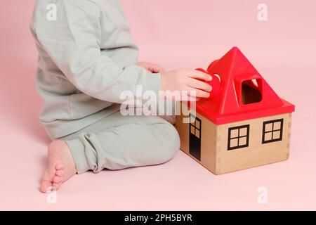 Happy toddler baby plays sorter with geometric shapes on studio pink background. Child boy plays educational toys. Kid age one year eight months Stock Photo