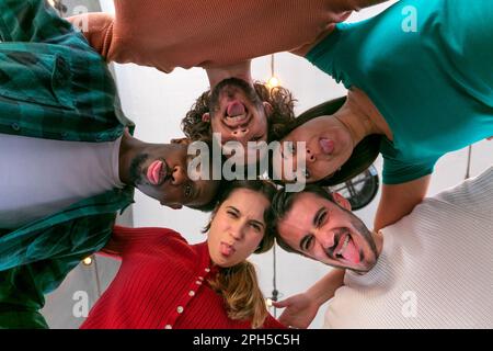 Happy multiethic students smiling and sticking out tongue at camera in a circle at the university, group of teenagers looking down Stock Photo