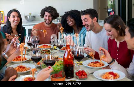 Friends are planning a dinner at home. They are laughing while eating spaghetti with tomato sauce Stock Photo