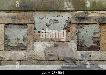 Background Photo of an Old Exterior Wall Built with Sandstone Blocks, Covered with Peeling Plaster. Grunge and Weathered Textured Surface Stock Photo