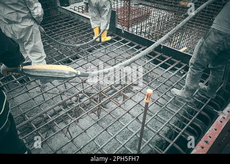 Construction workers dressed in protective workwear use concrete dipping compactor. Concrete casting and compaction. Using handheld cement vibrating m Stock Photo