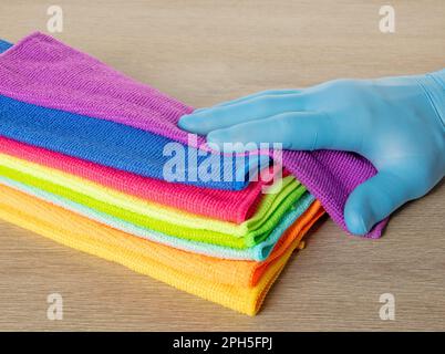 Hand in a blue glove selects a towel from a stack of bright microfiber towels for cleaning Stock Photo