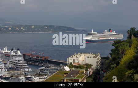 Cunard liner Queen Elizabeth anchored off Monaco, Monte Carlo.  Super yachts in the harbour foreground. Stock Photo