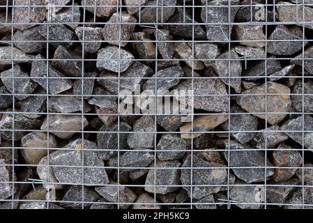 Mineral stones lie behind a metal grate. Wall of stones Stock Photo