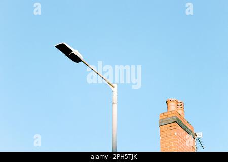 Minimalist photo of a street lamp and chimney from a nearby roof against a blue sky, England, UK, with copy space Stock Photo