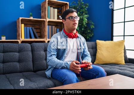 Down syndrome man playing video game sitting on sofa at home Stock Photo