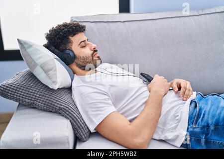 Young arab man listening to music sleeping on sofa at home Stock Photo