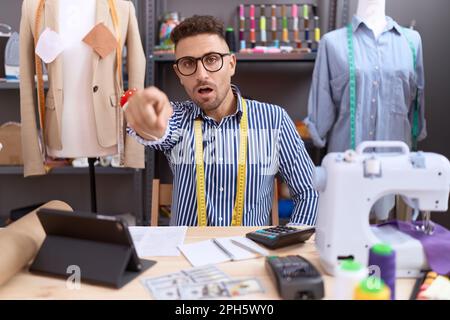Hispanic man with beard dressmaker designer working at atelier pointing displeased and frustrated to the camera, angry and furious with you Stock Photo