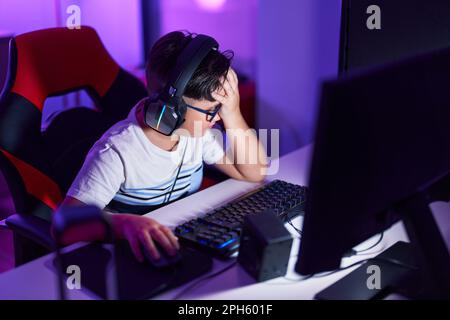 Adorable hispanic boy streamer stressed using computer at gaming room ...