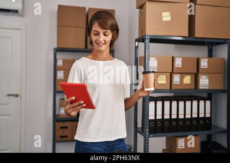 Young beautiful hispanic woman ecommerce business worker using touchpad drinking coffee at office Stock Photo